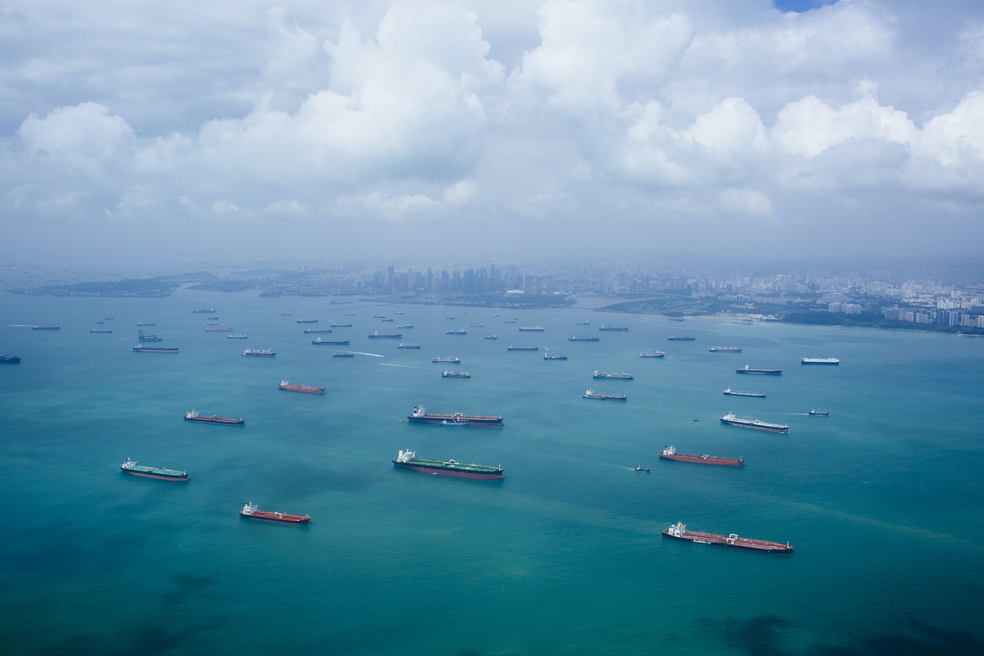 High angle view of barges and cargo ships in a bay, cityscape in the distance.